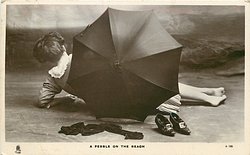 A PEBBLE ON THE BEACH young woman lies on beach behind umbrella