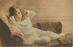 girl lying left on couch, facing left, looking forward, both hands in hair, right elbow rests on pillow