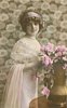 Image 1 - glamorous lady in dress with lace top & filmy shawl over her arm, bunch of roses in copper vase, looks at camera but body turned to right, right hand touches flowers