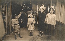 four children in room three stand facing front, boy on left faces right with sword in air boy & 2 girls face front standing at attention