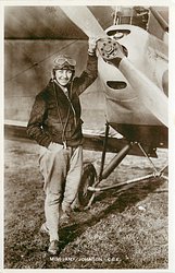 in flying gear, holding on to prop near its axle, right hand in pocket