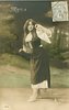 Image 1 - Mignon stands facing left, looking apprehensively back to right, her left arm raised