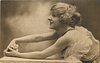 Image 1 - woman with flufy hair reaches arms across table left, rose in between her hands