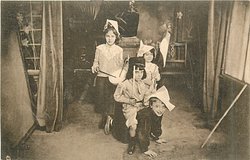 four children in room, 2 boys front one riding on others back, 2 girls behind, one playing drum