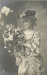 girl stands looking half left holding floral basket held in front of her
