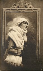 pretty girl with ermine fur & cap posed in front of framed mirror, she faces right looks partly right & up