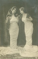 girl on right has arm behind other girl & leans toward her, both look down