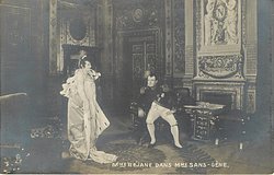 MME REJANE DANS MME. SANS-GENE elborately dressed actress stands left, man sits right