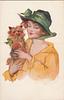 Image 1 - Woman in yellow dress, green ribbon and bow on hat holding dog,