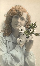 girl faces camera, holds flowers to her left cheek, looks upwards at camera