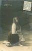 Image 1 - Mignon kneels facing right, looking front, right hand on left knee