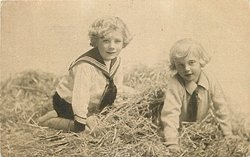 two boys play in straw, both on hands & knees, looking forward