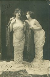 girl on right has arm behind other girl & leans toward her staring at the others eyes-closed facial expression