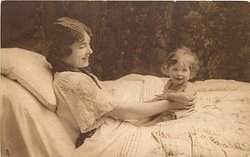 mother lying in bed smiling at baby sitting at arms length in front of her