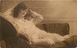 girl lying left on couch, both hands at sides of her head, right elbow rests on pillow