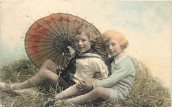 two boys play in straw, looking forward, parasol behind, handle to left of boy on left