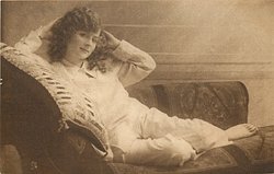girl lying left on couch, both hands at sides of her head, right elbow rests on pillow