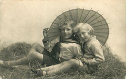 two boys play in straw, looking forward, parasol behind, handle between boys