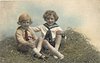 Image 1 - two boys play in straw, both sit cross-legged, looking forward