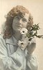 Image 1 - girl faces camera, holds flowers to her left cheek, looks upwards at camera