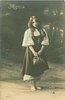 Image 3 - Mignon stands holding bag, looking down