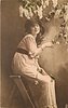 Image 2 - girl sits on stepladder facing right, looking front, touching lilac in front of her with her right hand & holding single rose on her lap with her left