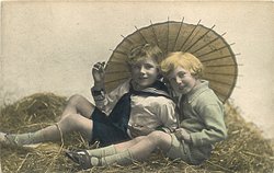 two boys play in straw, looking forward, parasol behind, handle between boys